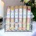 Assorted bath salts by Whole Self Aromatherapy in test tubes on elegant white linen, with a candle softly glowing in the background.
